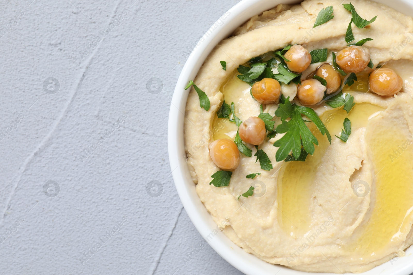 Photo of Delicious hummus with olive oil, chickpeas and parsley in bowl on grey textured table, top view. Space for text