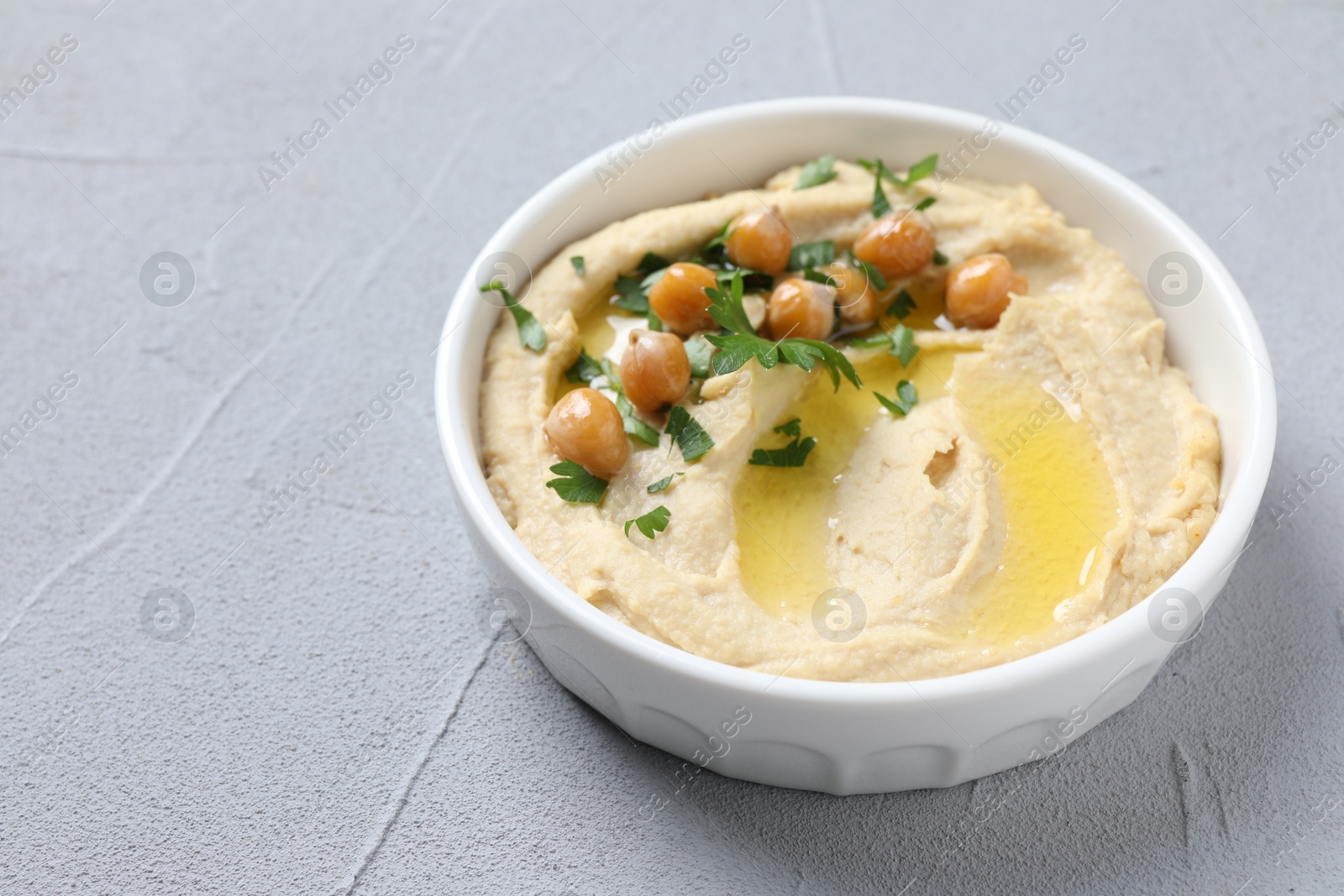 Photo of Delicious hummus with olive oil, chickpeas and parsley in bowl on grey textured table