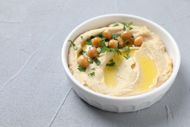 Photo of Delicious hummus with olive oil, chickpeas and parsley in bowl on grey textured table