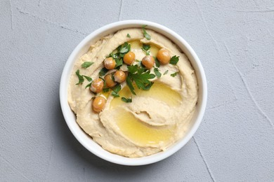 Photo of Delicious hummus with olive oil, chickpeas and parsley in bowl on grey textured table, top view