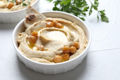 Photo of Delicious hummus with olive oil, chickpeas and pita in bowl on light textured table