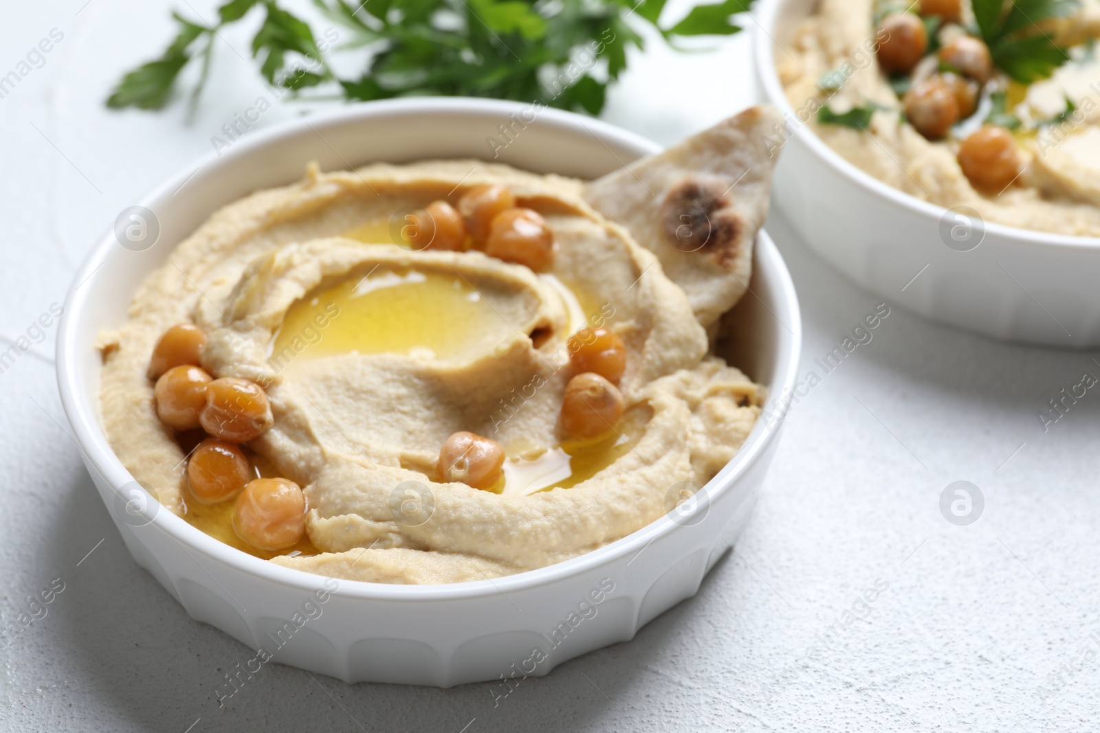 Photo of Delicious hummus with olive oil, chickpeas and pita in bowl on light textured table