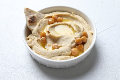 Photo of Delicious hummus with olive oil, chickpeas and pita in bowl on light textured table