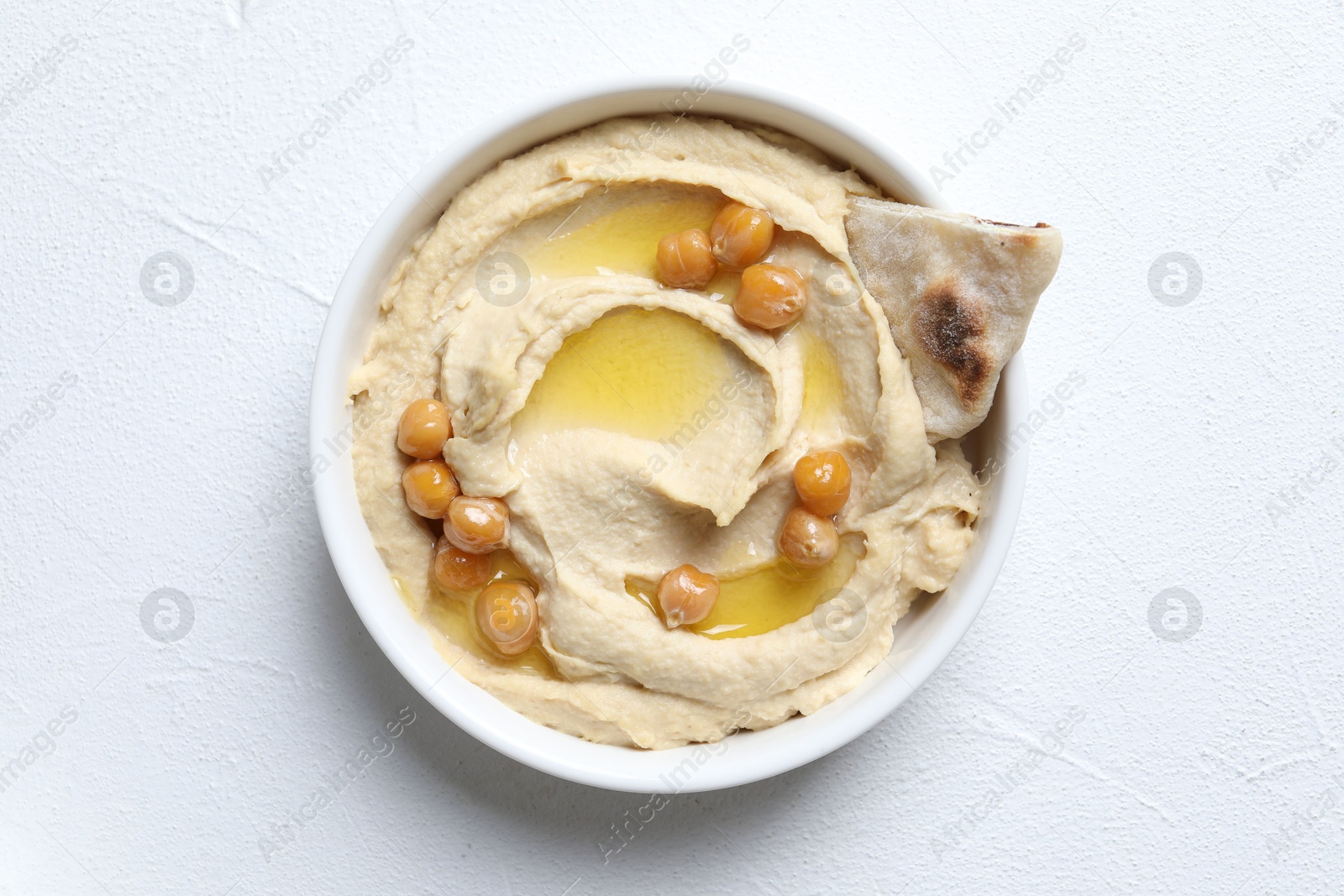 Photo of Delicious hummus with olive oil, chickpeas and pita in bowl on light textured table, top view