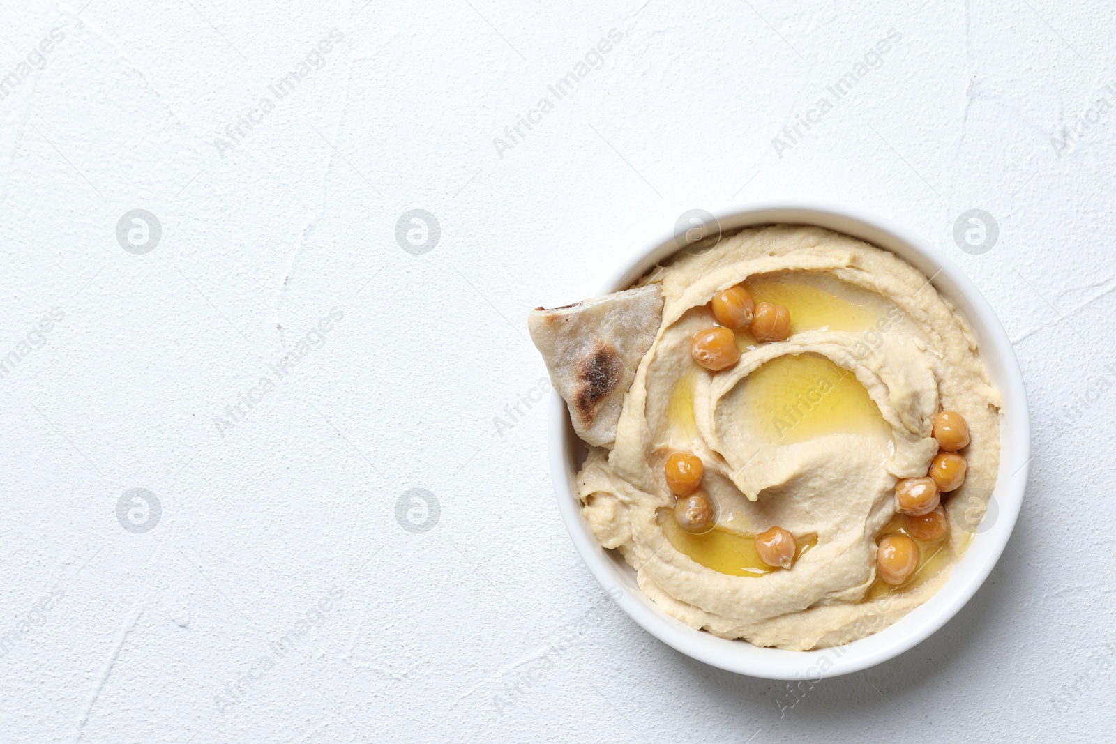 Photo of Delicious hummus with olive oil, chickpeas and pita in bowl on light textured table, top view. Space for text