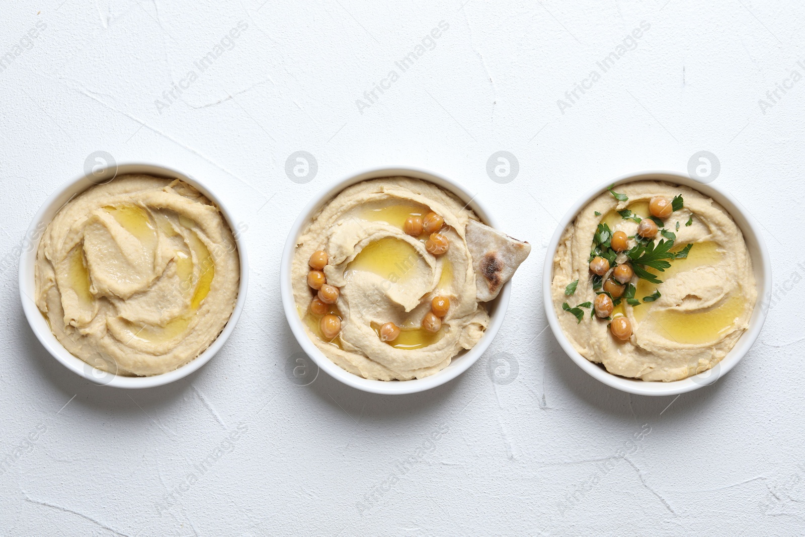 Photo of Delicious hummus with olive oil, chickpeas and pita in bowls on light textured table, flat lay