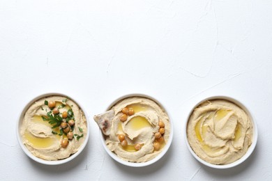 Delicious hummus with olive oil, chickpeas and pita in bowls on light textured table, flat lay. Space for text