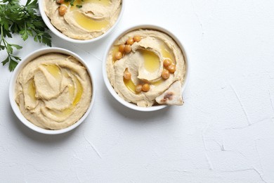 Delicious hummus with olive oil, chickpeas and pita in bowls on light textured table, flat lay. Space for text