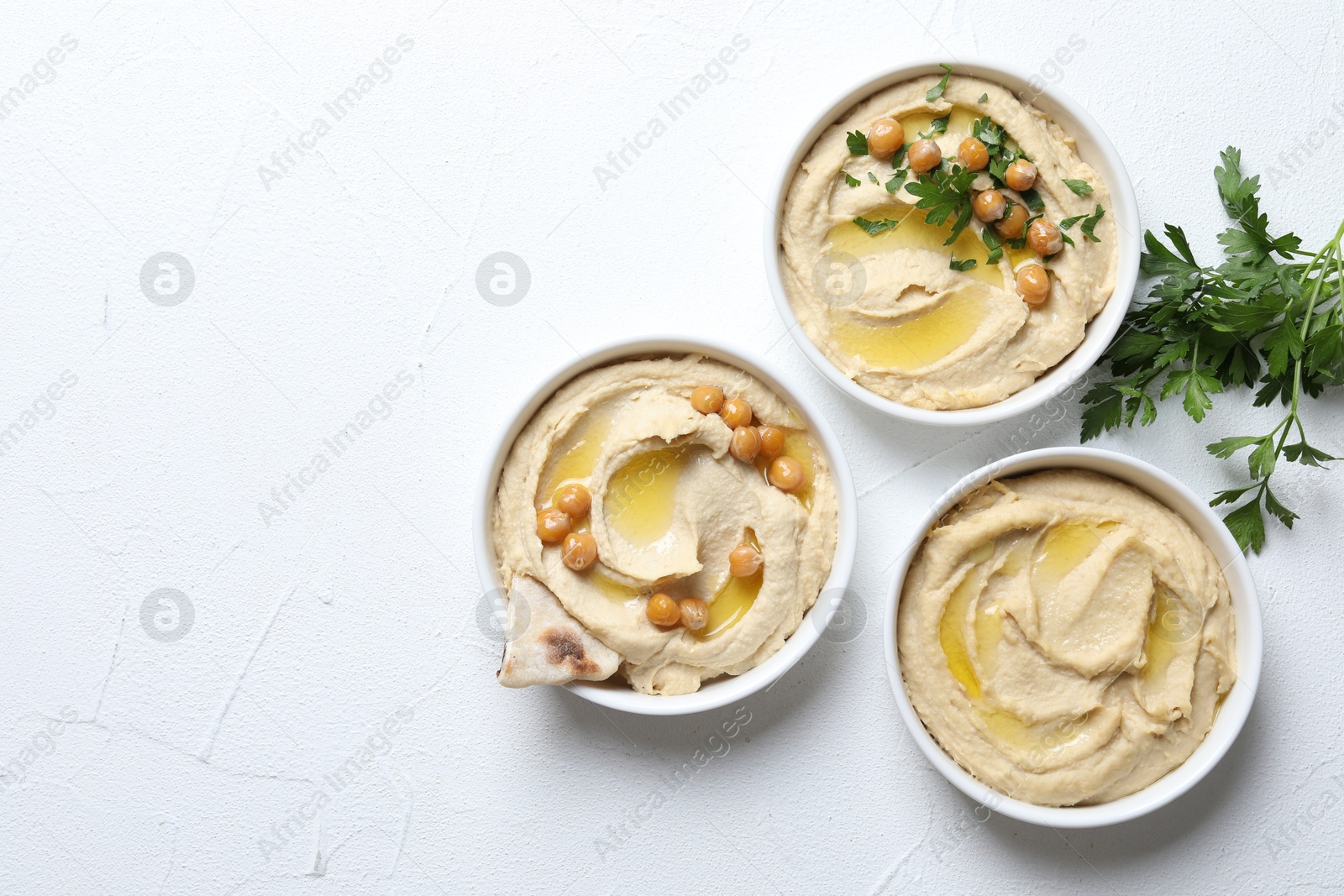 Photo of Delicious hummus with olive oil, chickpeas and pita in bowls on light textured table, flat lay. Space for text