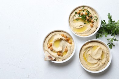 Delicious hummus with olive oil, chickpeas and pita in bowls on light textured table, flat lay. Space for text