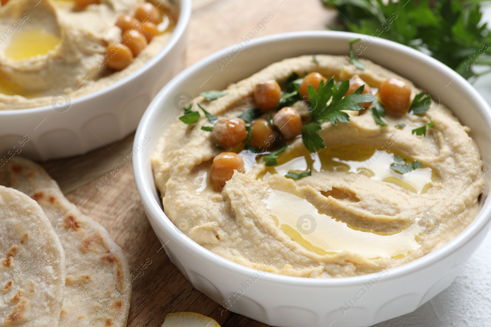 Photo of Delicious hummus with olive oil, chickpeas and parsley served on light table