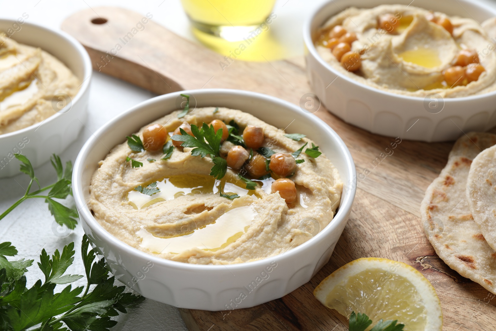 Photo of Delicious hummus with olive oil, chickpeas and parsley served on light table