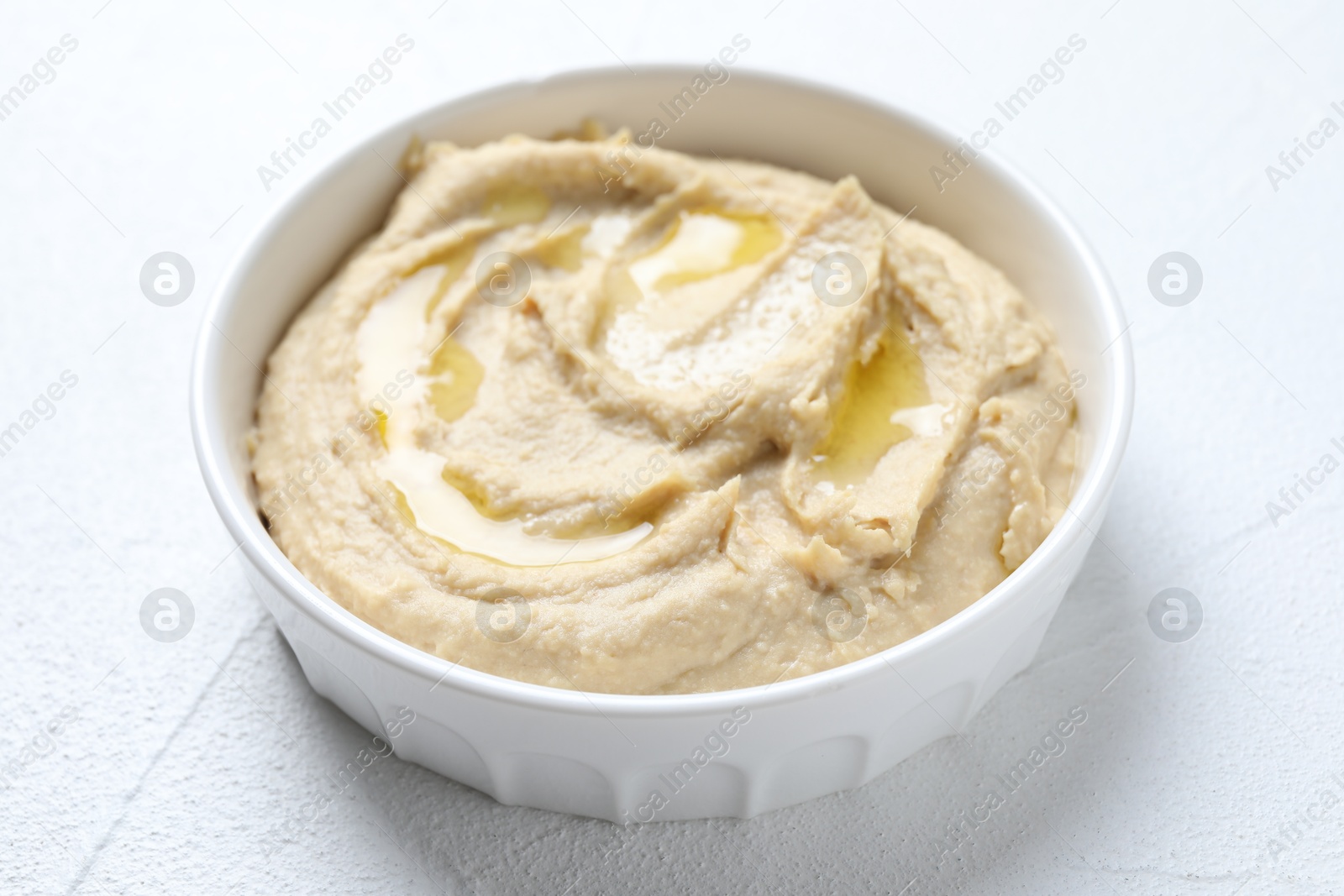 Photo of Delicious hummus with olive oil in bowl on white textured table, closeup