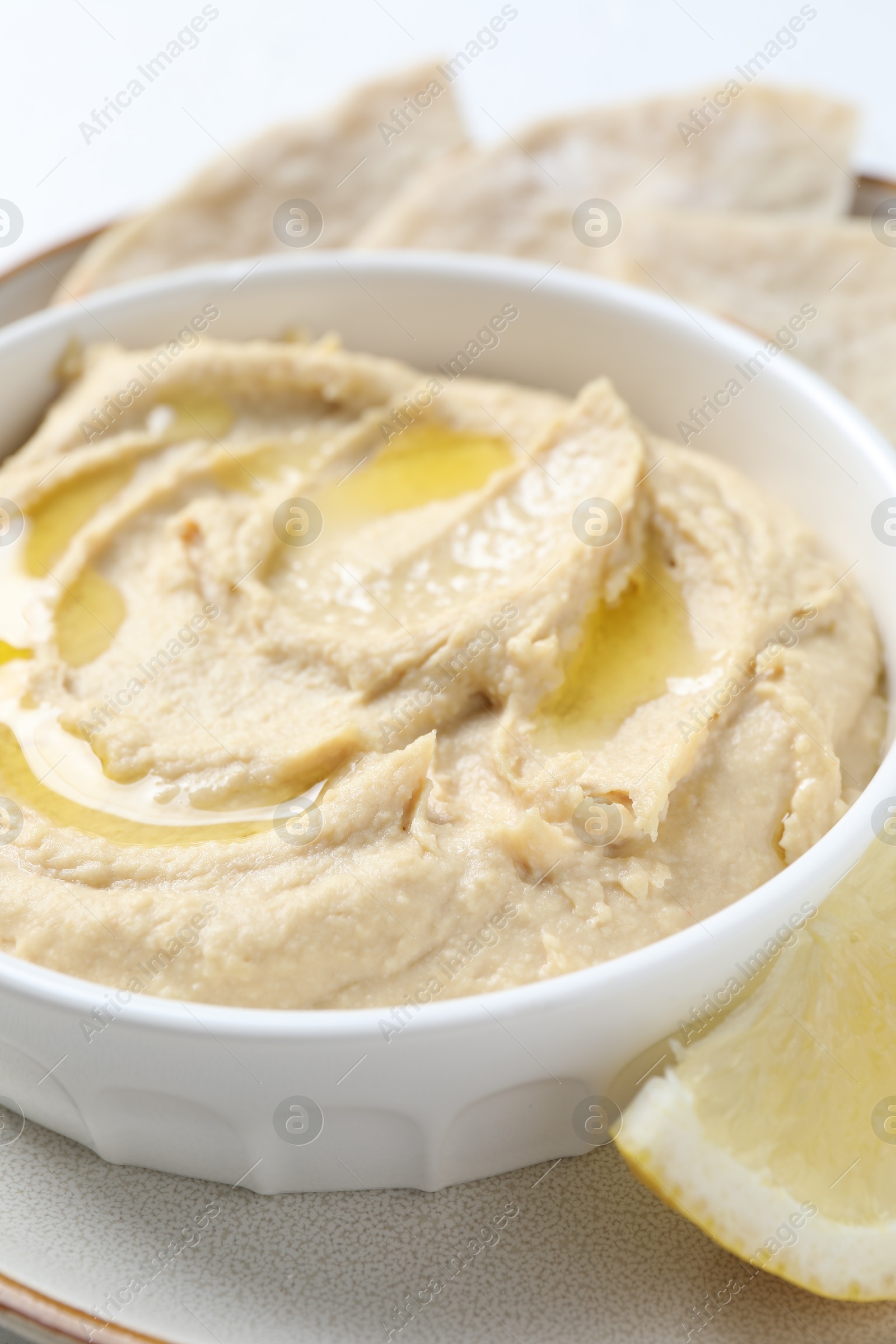 Photo of Delicious hummus with olive oil in bowl and lemon on white table, closeup