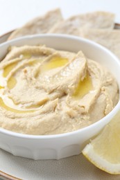 Photo of Delicious hummus with olive oil in bowl and lemon on white table, closeup