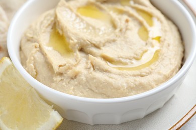 Photo of Delicious hummus with olive oil in bowl and lemon on white table, closeup