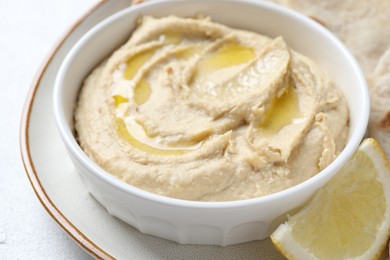 Photo of Delicious hummus with olive oil in bowl and lemon on white table, closeup