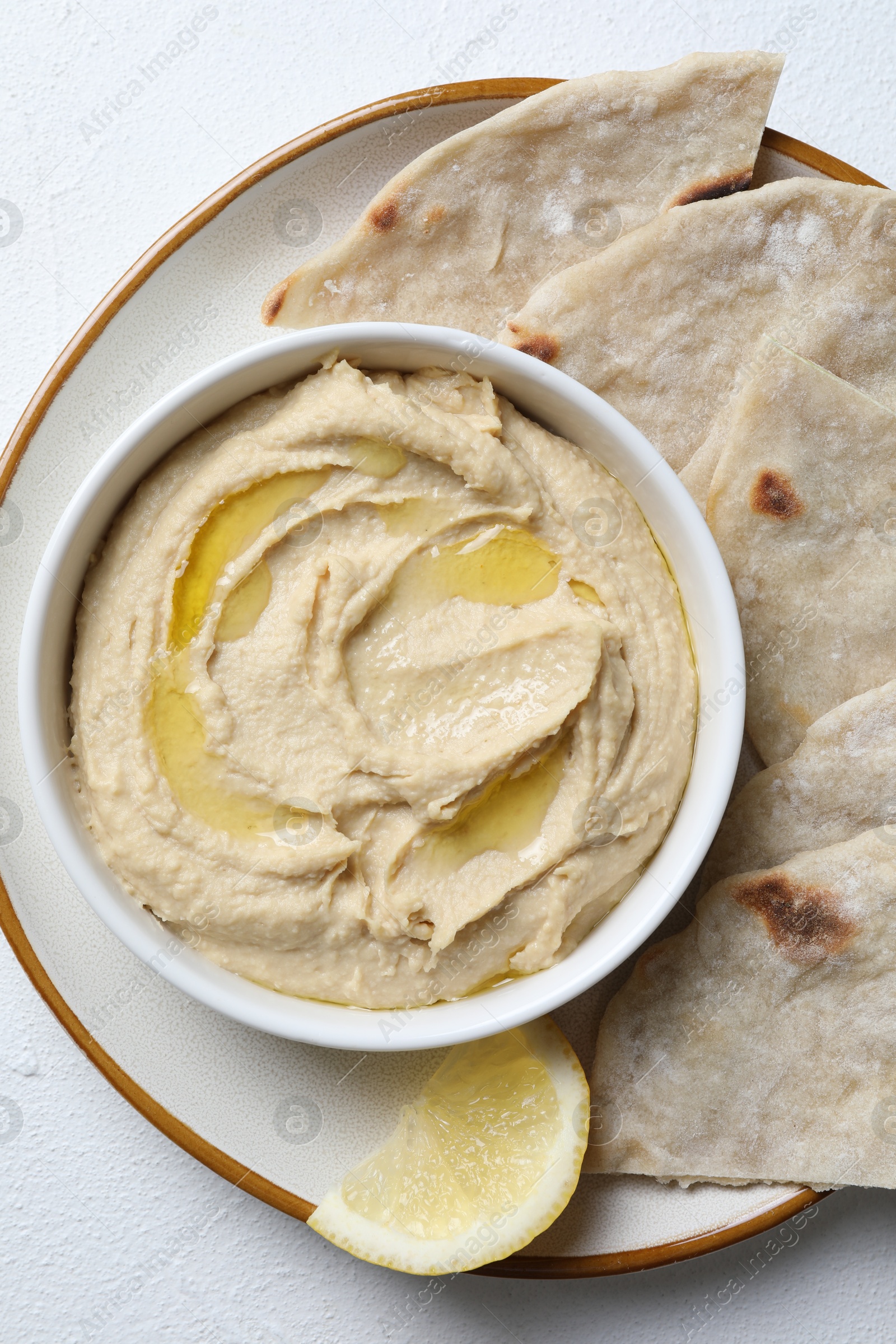 Photo of Delicious hummus with olive oil in bowl and pita on light textured table, top view