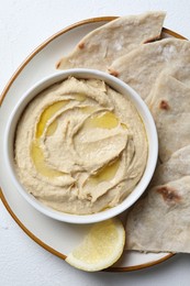 Delicious hummus with olive oil in bowl and pita on light textured table, top view