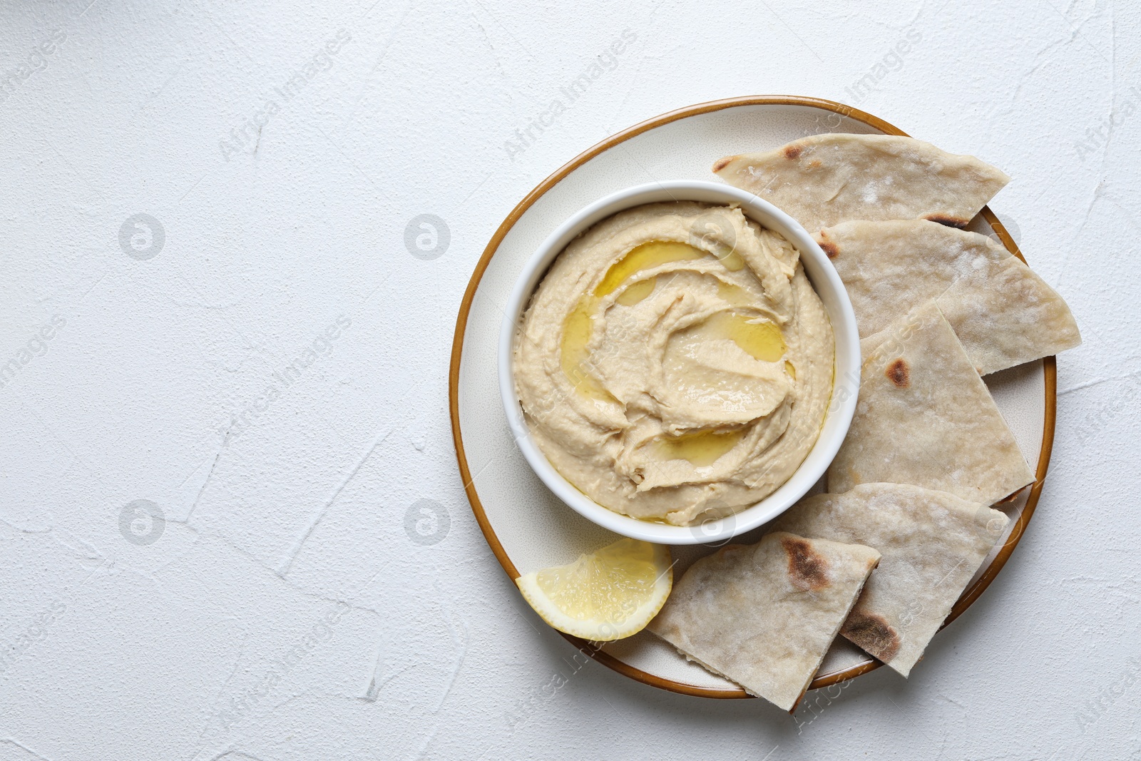 Photo of Delicious hummus with olive oil in bowl and pita on light textured table, top view. Space for text