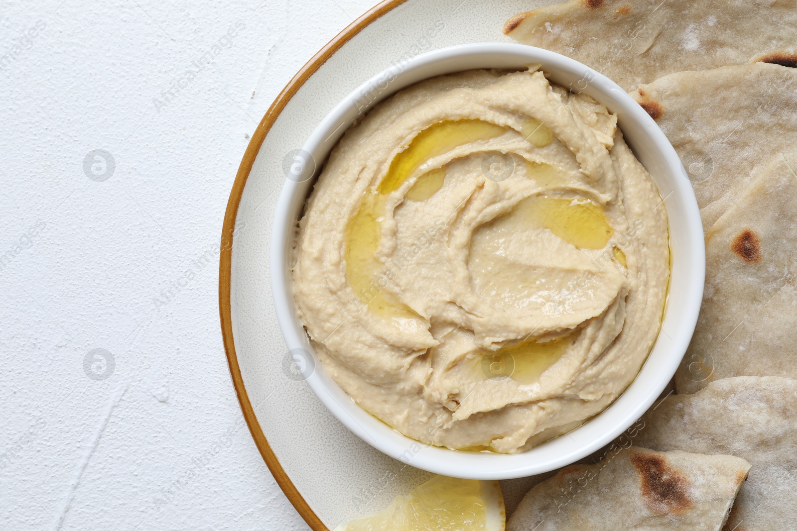 Photo of Delicious hummus with olive oil in bowl and pita on light textured table, top view