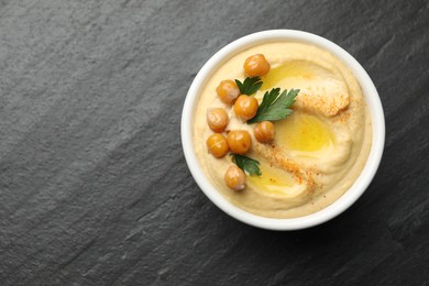 Photo of Delicious hummus with olive oil, chickpeas and parsley in bowl on grey textured table, top view. Space for text