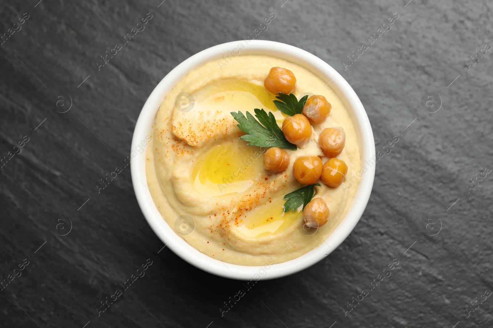 Photo of Delicious hummus with olive oil, chickpeas and parsley in bowl on grey textured table, top view