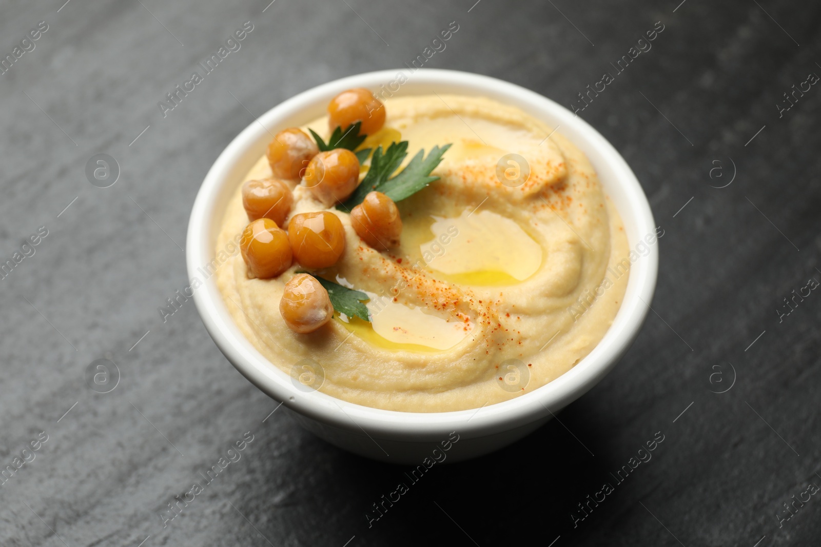 Photo of Delicious hummus with olive oil, chickpeas and parsley in bowl on grey table