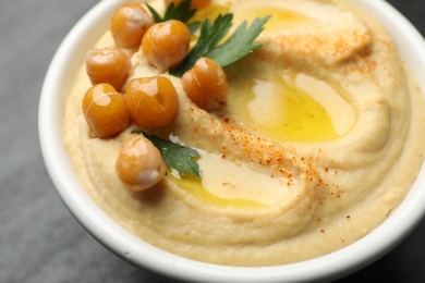 Photo of Delicious hummus with olive oil, chickpeas and parsley in bowl on grey table, closeup