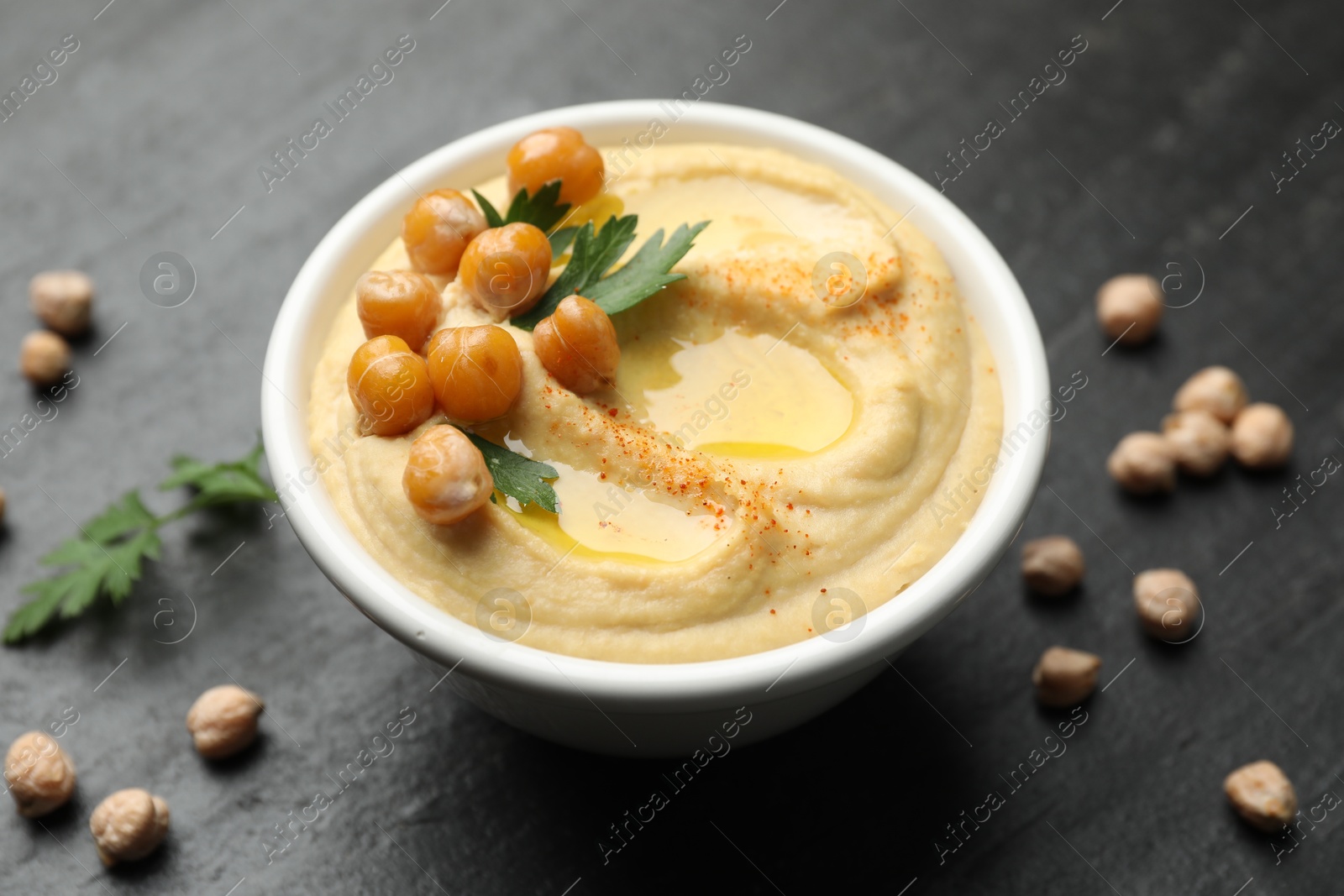 Photo of Delicious hummus with olive oil, chickpeas and parsley on grey table