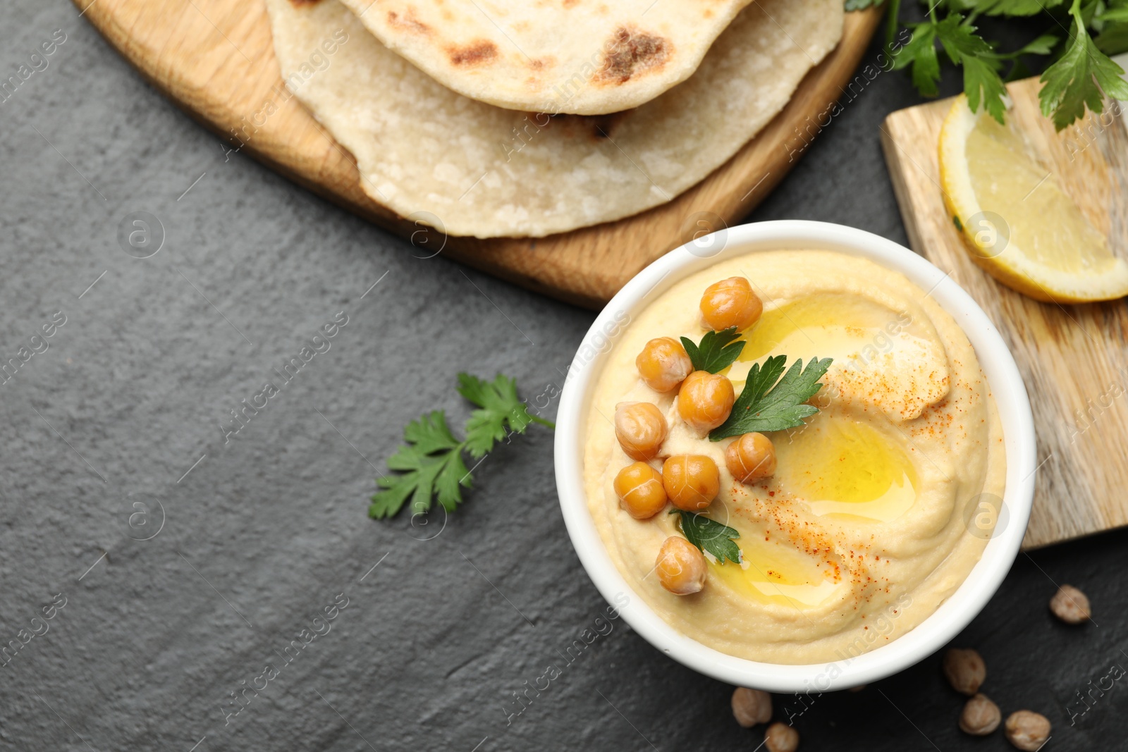 Photo of Delicious hummus with olive oil and chickpeas served on grey textured table, flat lay. Space for text