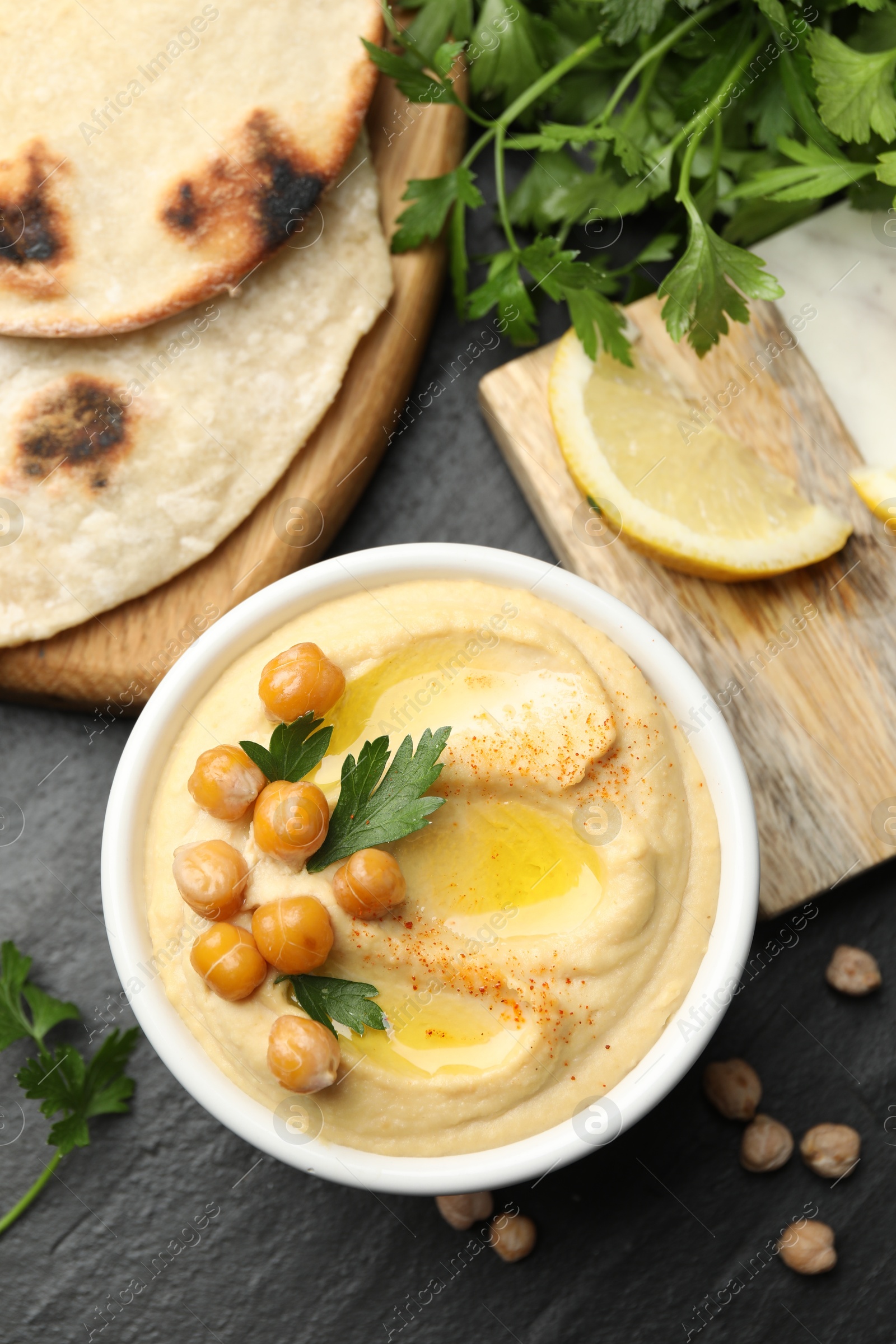 Photo of Delicious hummus with olive oil and chickpeas served on grey textured table, flat lay