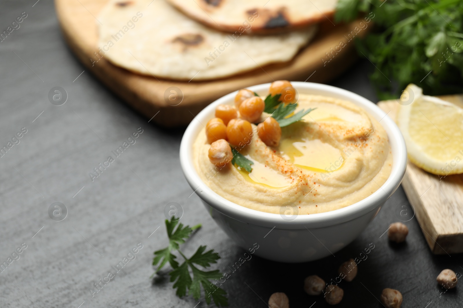 Photo of Delicious hummus with olive oil and chickpeas served on grey table