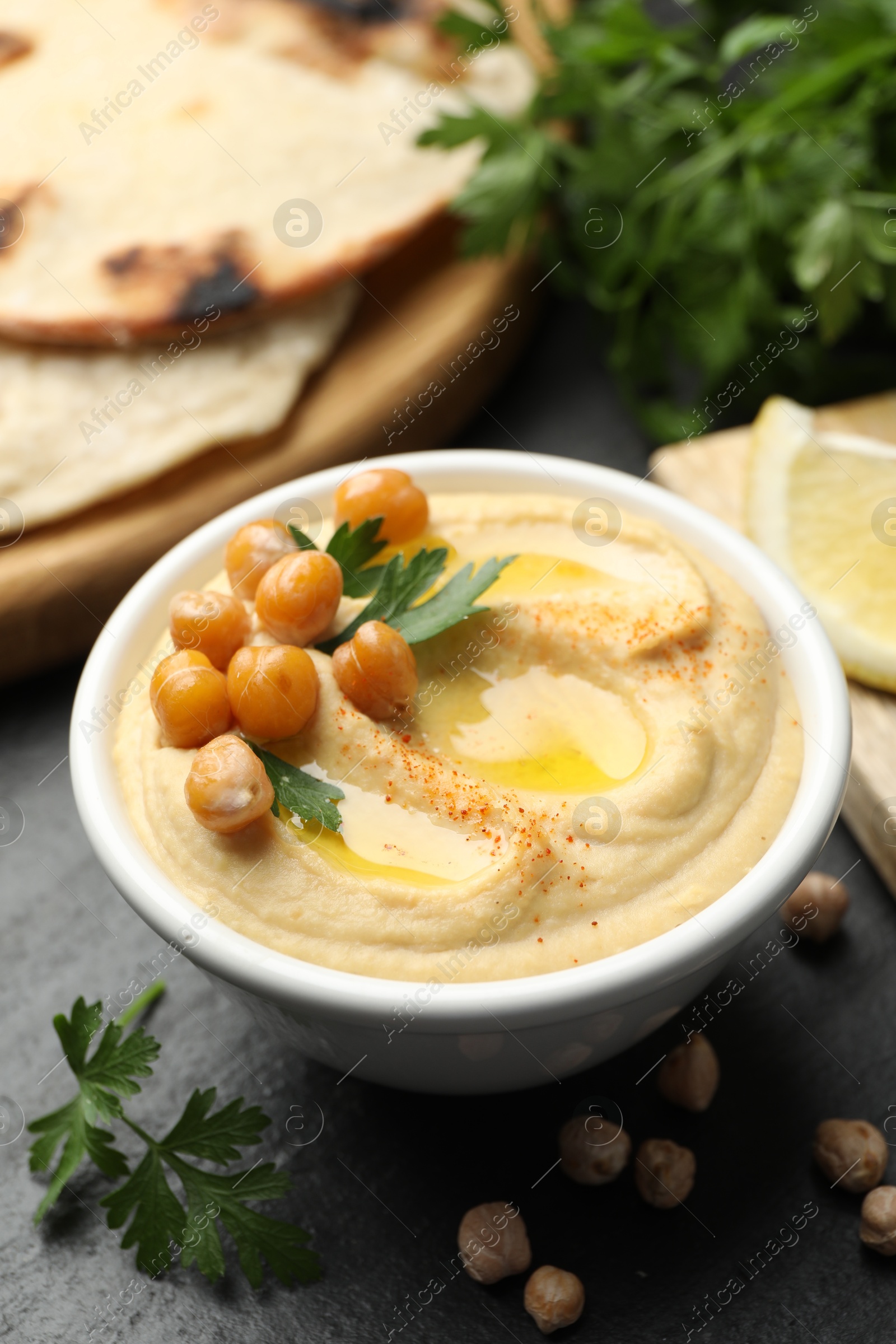 Photo of Delicious hummus with olive oil and chickpeas served on grey table