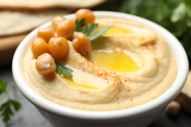 Photo of Delicious hummus with olive oil, chickpeas and parsley in bowl on grey table, closeup