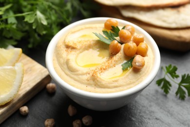 Photo of Delicious hummus with olive oil and chickpeas in bowl served on grey table, closeup