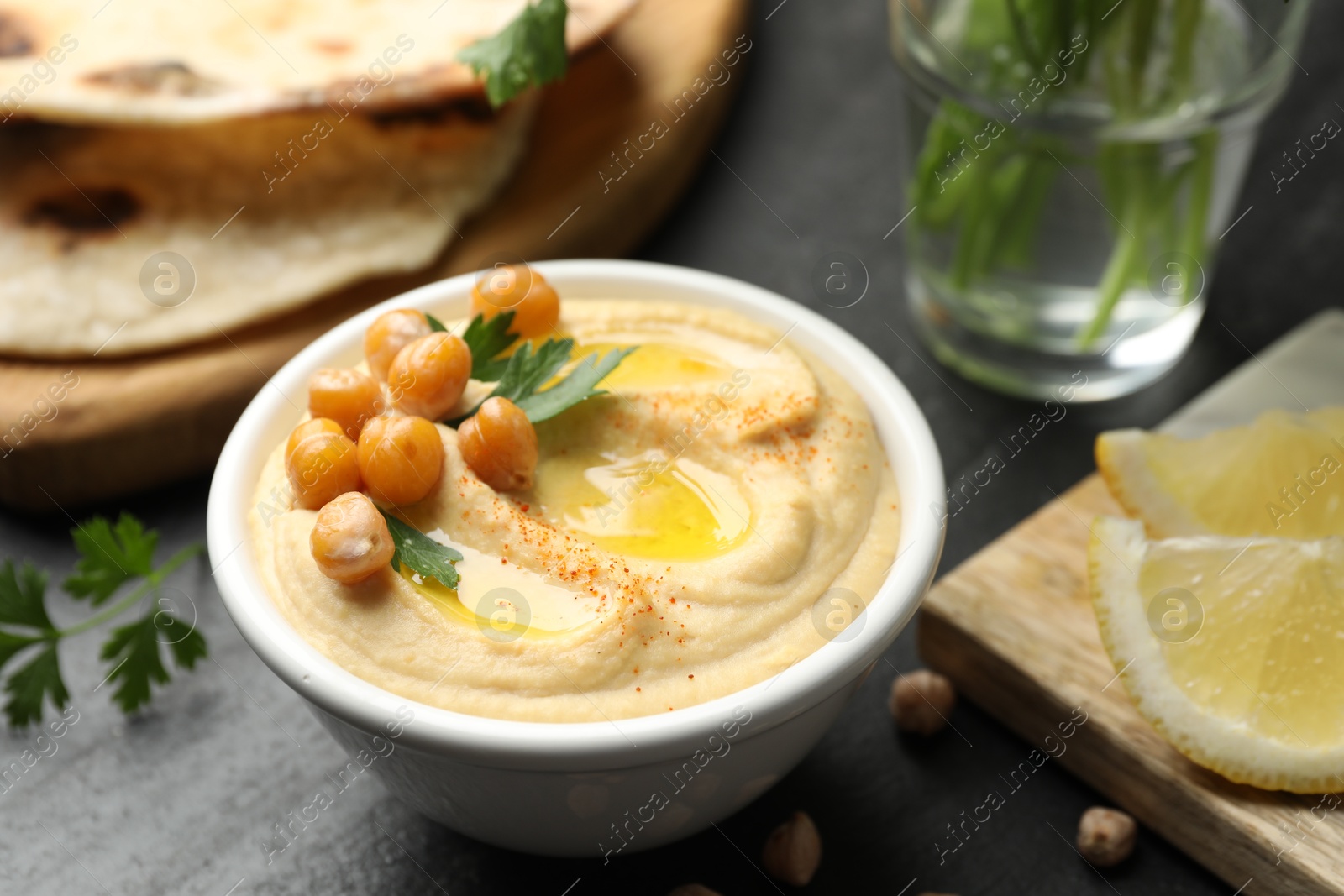 Photo of Delicious hummus with olive oil and chickpeas in bowl served on grey table, closeup