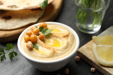 Photo of Delicious hummus with olive oil and chickpeas in bowl served on grey table, closeup