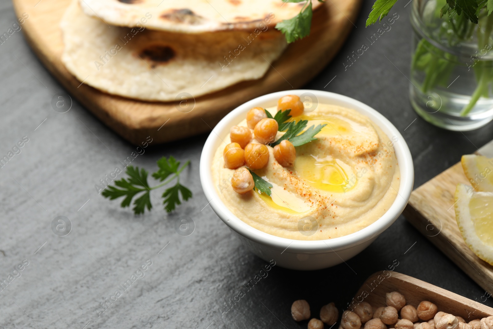 Photo of Delicious hummus with olive oil and chickpeas in bowl served on grey table