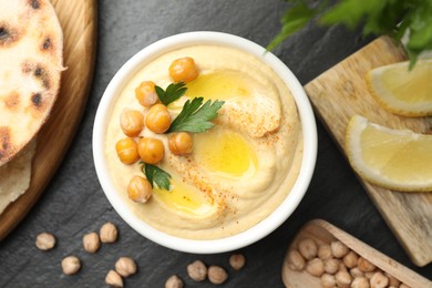 Photo of Delicious hummus with olive oil and chickpeas served on grey textured table, flat lay