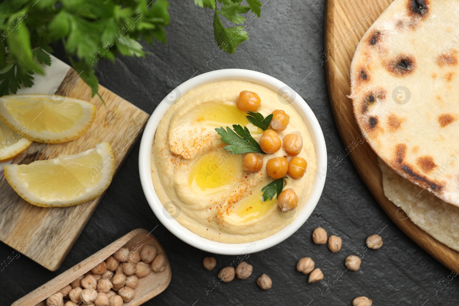 Photo of Delicious hummus with olive oil and chickpeas served on grey textured table, flat lay