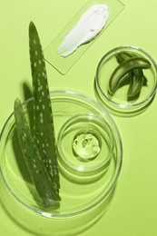 Photo of Petri dishes with fresh leaves and cosmetic products on green background, flat lay