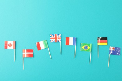 Small paper flags of different countries on light blue background, flat lay