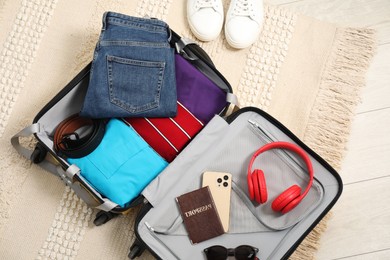 Open suitcase with traveler's belongings on floor, flat lay