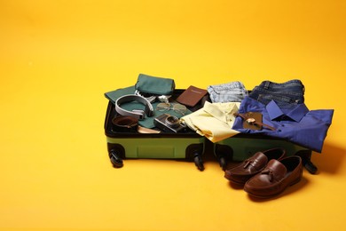 Open suitcase with traveler's belongings on yellow background, space for text