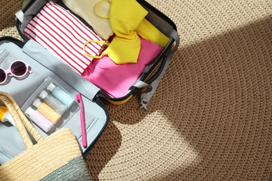 Open suitcase with traveler's belongings on rug, top view. Space for text