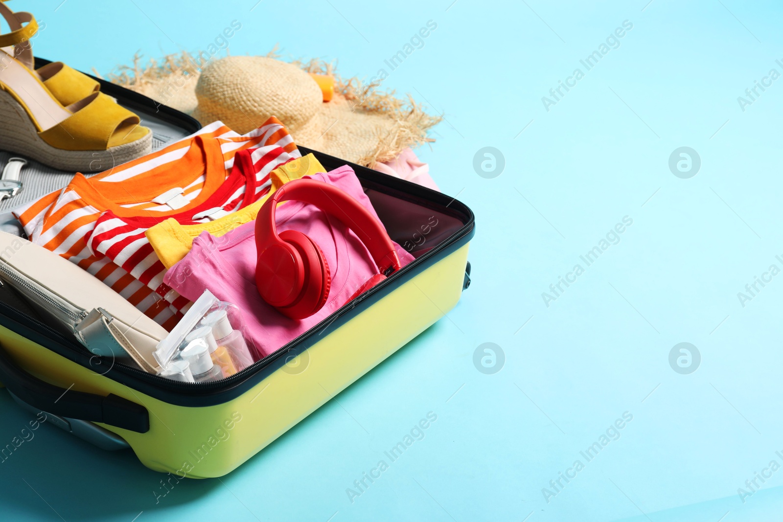 Photo of Open suitcase with traveler's belongings on light blue background, space for text