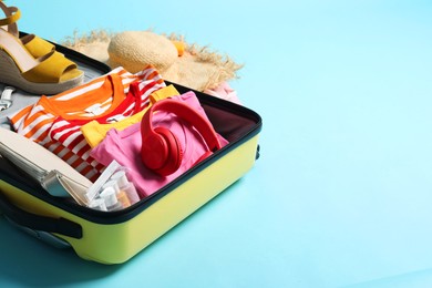 Photo of Open suitcase with traveler's belongings on light blue background, space for text