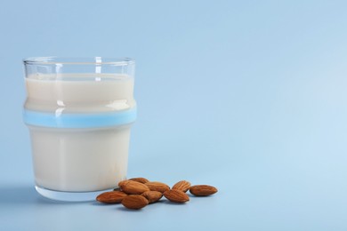 Photo of Fresh almond milk in glass and nuts on light blue background, space for text