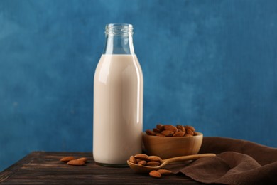 Photo of Fresh almond milk in glass bottle, nuts and spoon on wooden table